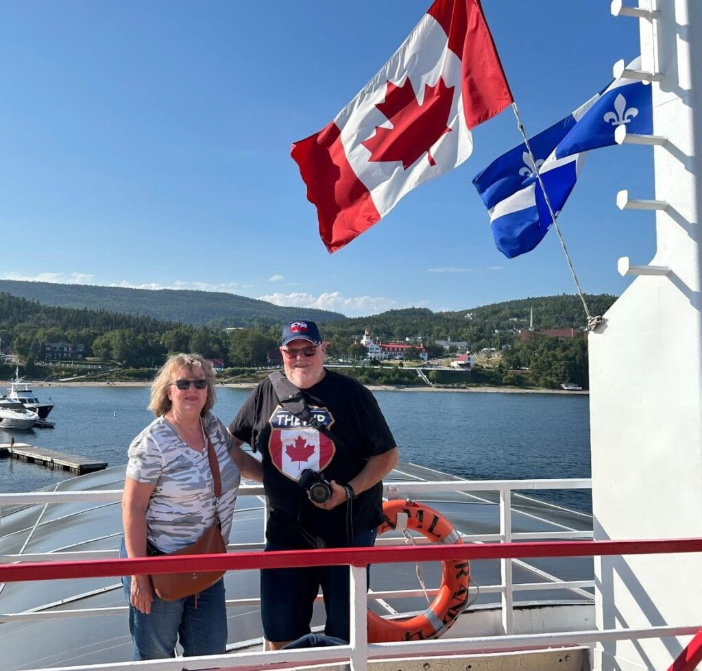 Couple on ferry deck during Canadian RV trip with flags in background.
