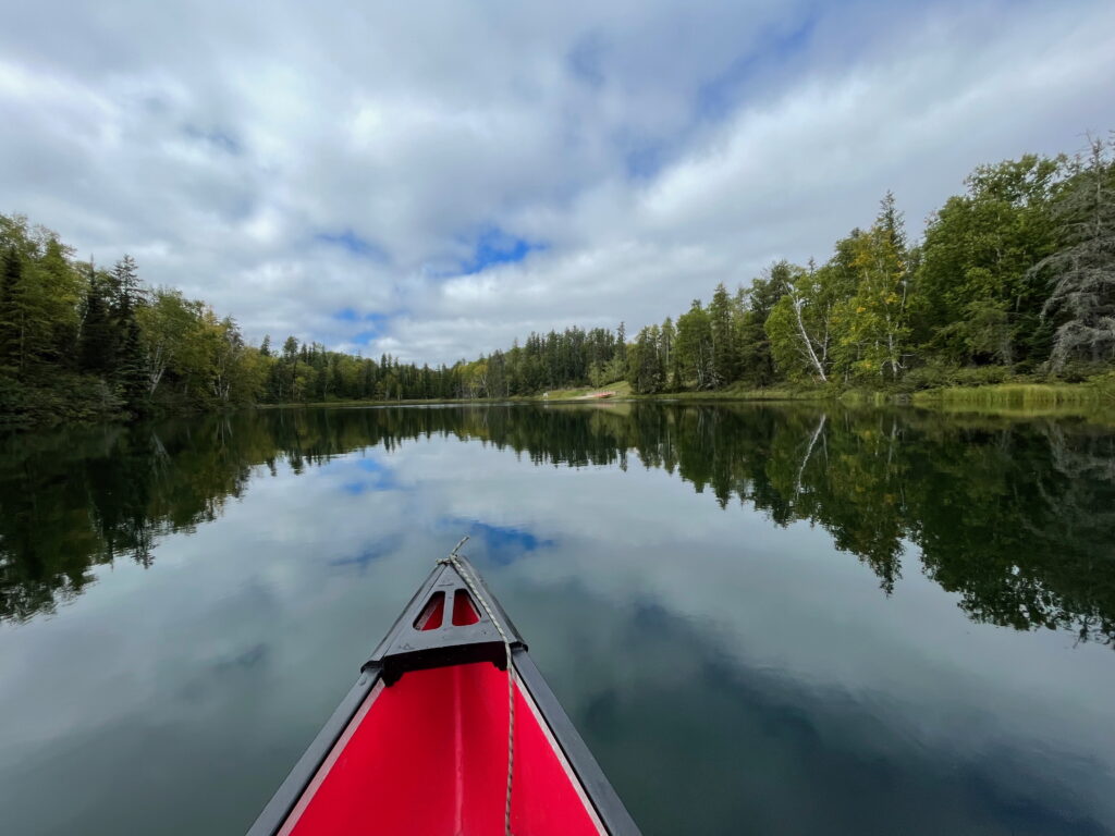 A red canoe on green lake surrounded by trees.